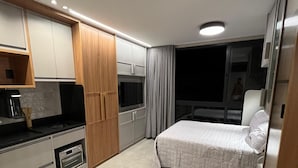 Habitación de hotel compacta con kitchenette, cama, sofá y una pequeña mesa.