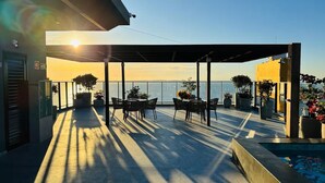 Una terraza en la azotea con zona de estar cubierta, piscina y vista al mar.