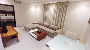 A modern hotel room with a sofa, a wooden coffee table, a small table, and a bed with a headboard.