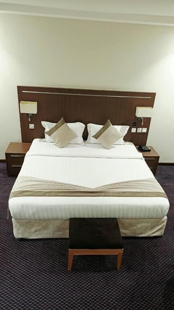 A hotel room with a large bed, two bedside tables, and a small stool.