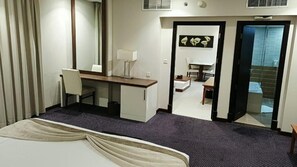 A hotel room with a bed, a desk, a chair, a mirror, and a bathroom visible through an open door. - Doolve Al Khobar (Al Khobar)