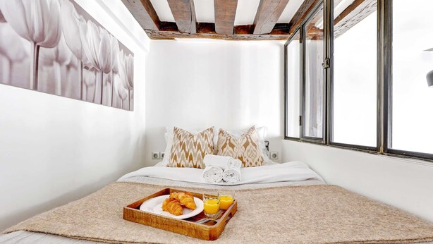 A bedroom with a bed, pillows, a tray with croissants and orange juice, and a large window. - Cozy Stay for 4 in the Heart (Paris)
