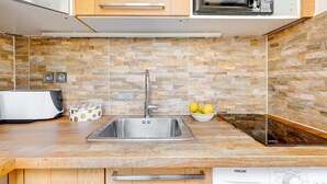 A kitchen with a stainless steel sink, a microwave, and a built-in oven. There is a toaster and a bowl of fruit on the counter. - Cozy Stay for 4 in the Heart (Paris)
