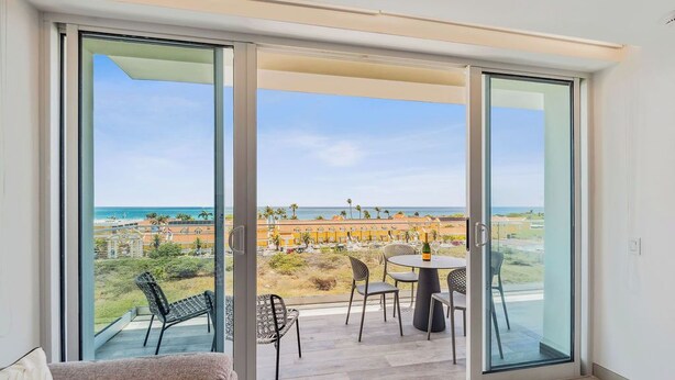 A balcony with a table and chairs, overlooking a beach and ocean.