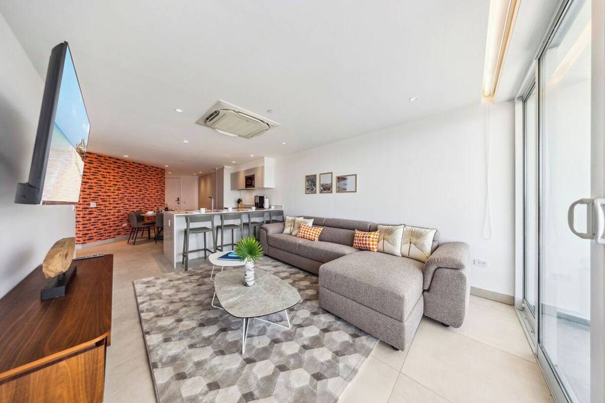 Una sala de estar moderna con un sofá modular gris, una mesa de centro y un televisor sobre un mueble de madera.