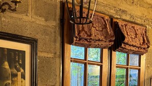 A rustic kitchen with a wooden counter, a framed vintage wine bottle photo, a hanging light fixture, and a window with a view of greenery. - Warm Montana Studio, Forest 1, 10' from downtown, (San Carlos de Bariloche)