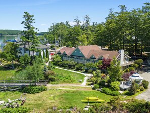 A large, multi-story building with a green roof, surrounded by lush greenery and a lake view.