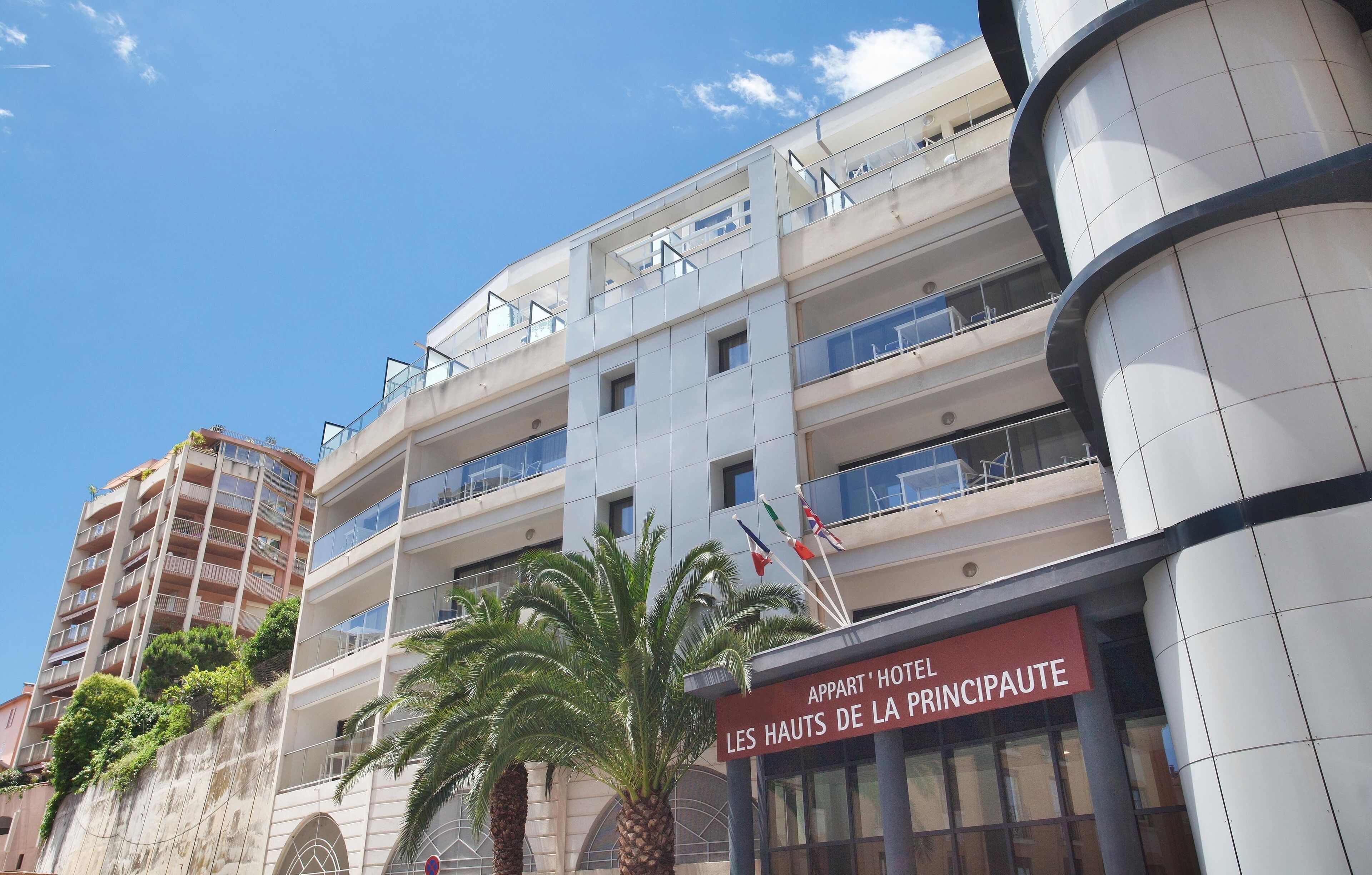 Um hotel com vários andares e varandas, com uma placa que diz 'Les Hauts de la Principaute'.