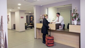 A reception area with a receptionist, a desk, a large mirror, and a plant. - T2 charmant en centre-ville, près des commerces (Strasbourg)