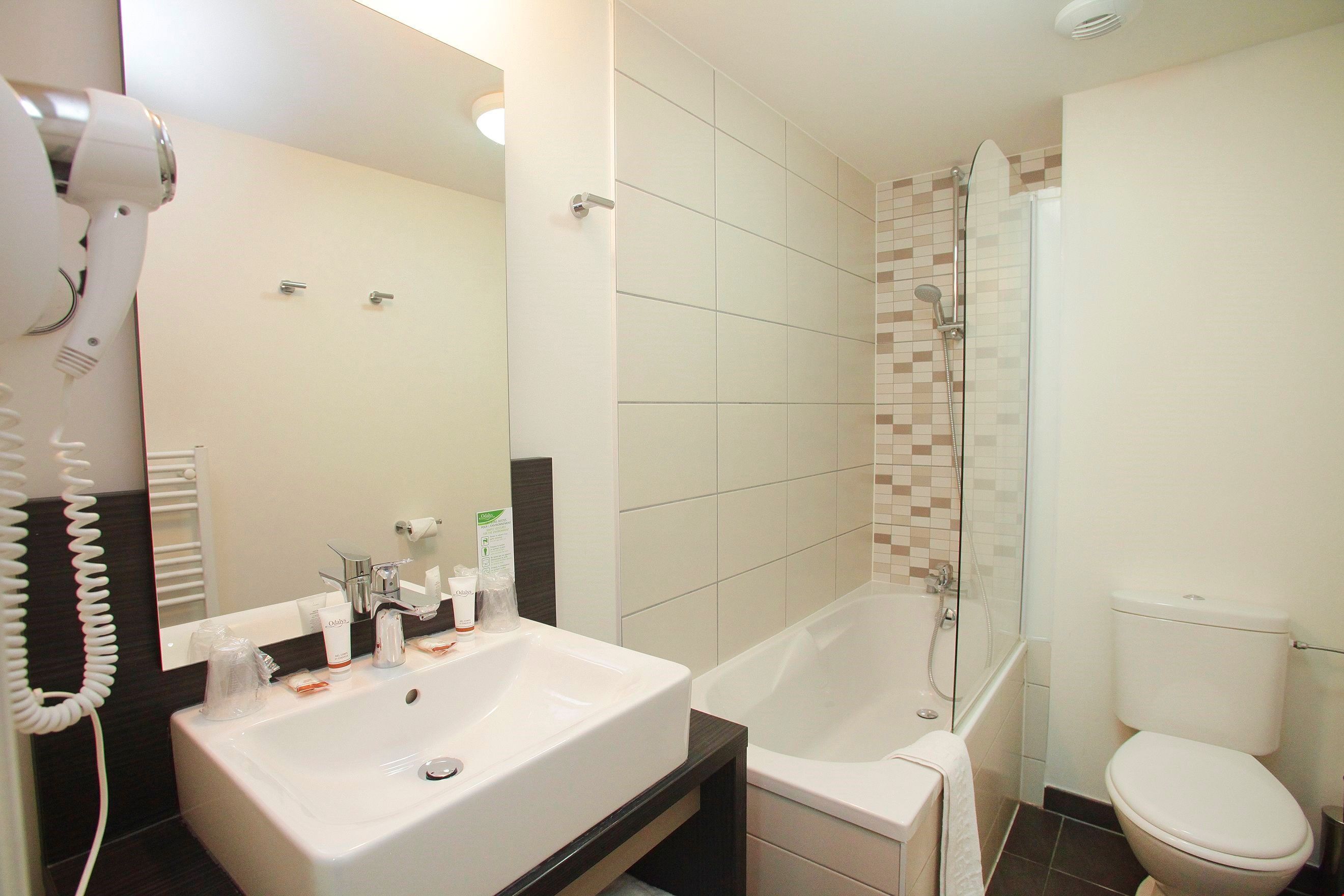 Une salle de bain équipée d’un lavabo, d’un miroir, d’un sèche-cheveux et d’un espace douche.