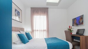 A hotel room with a bed, a desk with a laptop, a chair, a window with curtains, and a framed picture on the wall. - Chambre twin confortable à 10 min du centre ville (Orleans)