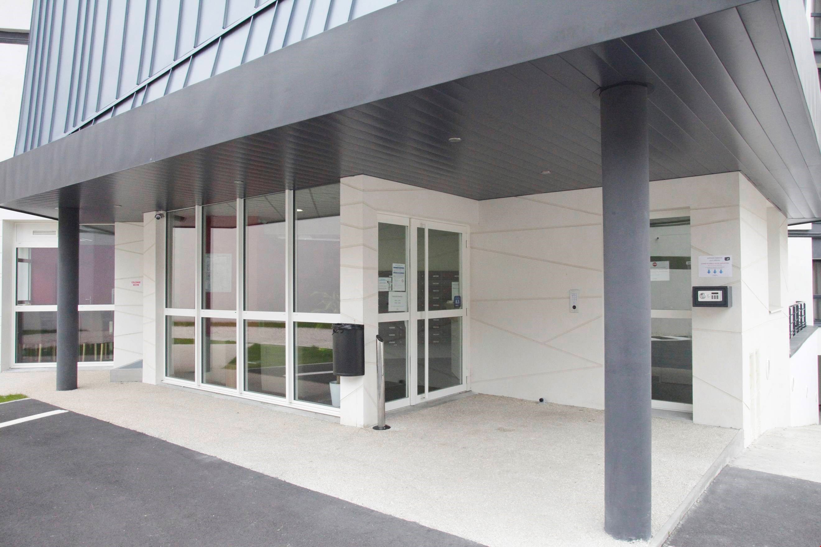 A modern building entrance with glass doors, a metal roof, and a concrete floor.