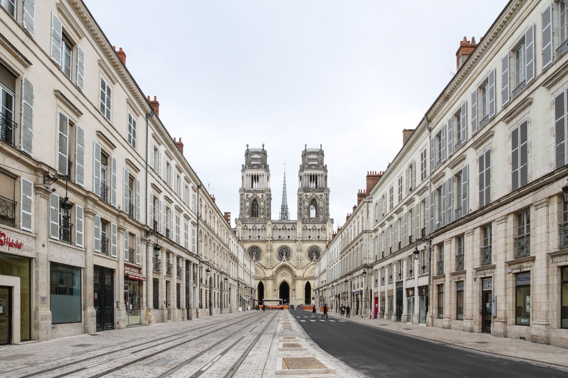 Uma rua que conduz a uma grande catedral com duas torres, ladeada por edifícios históricos com fachadas e persianas uniformes.