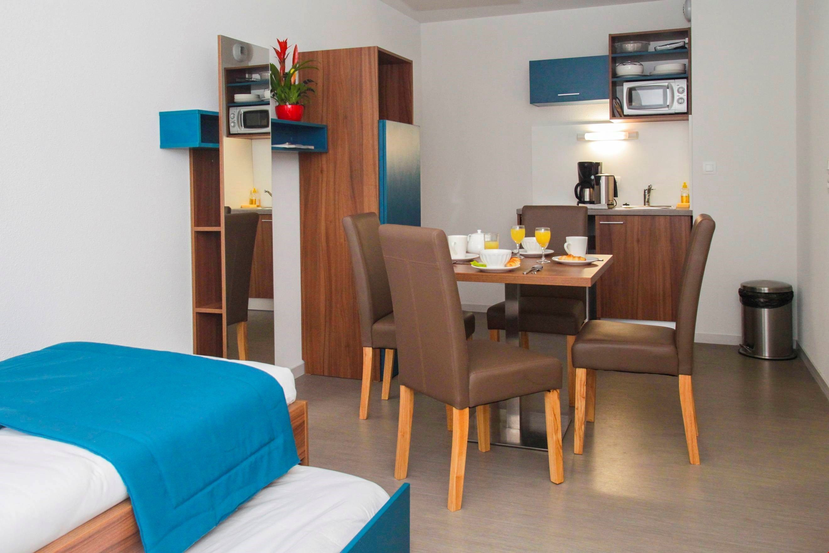 Habitación de hotel compacta con cama, mesa de comedor con sillas, microondas y una pequeña kitchenette.