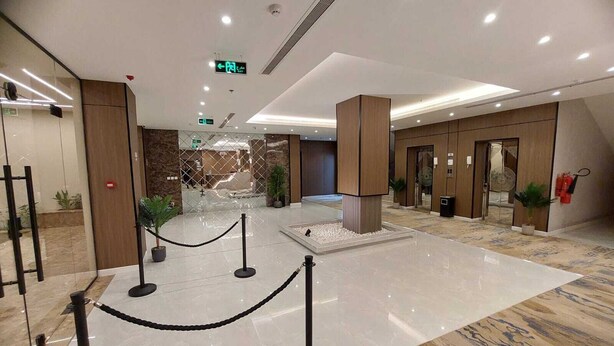 A modern lobby with a marble floor, a central water feature, and a glass partition.