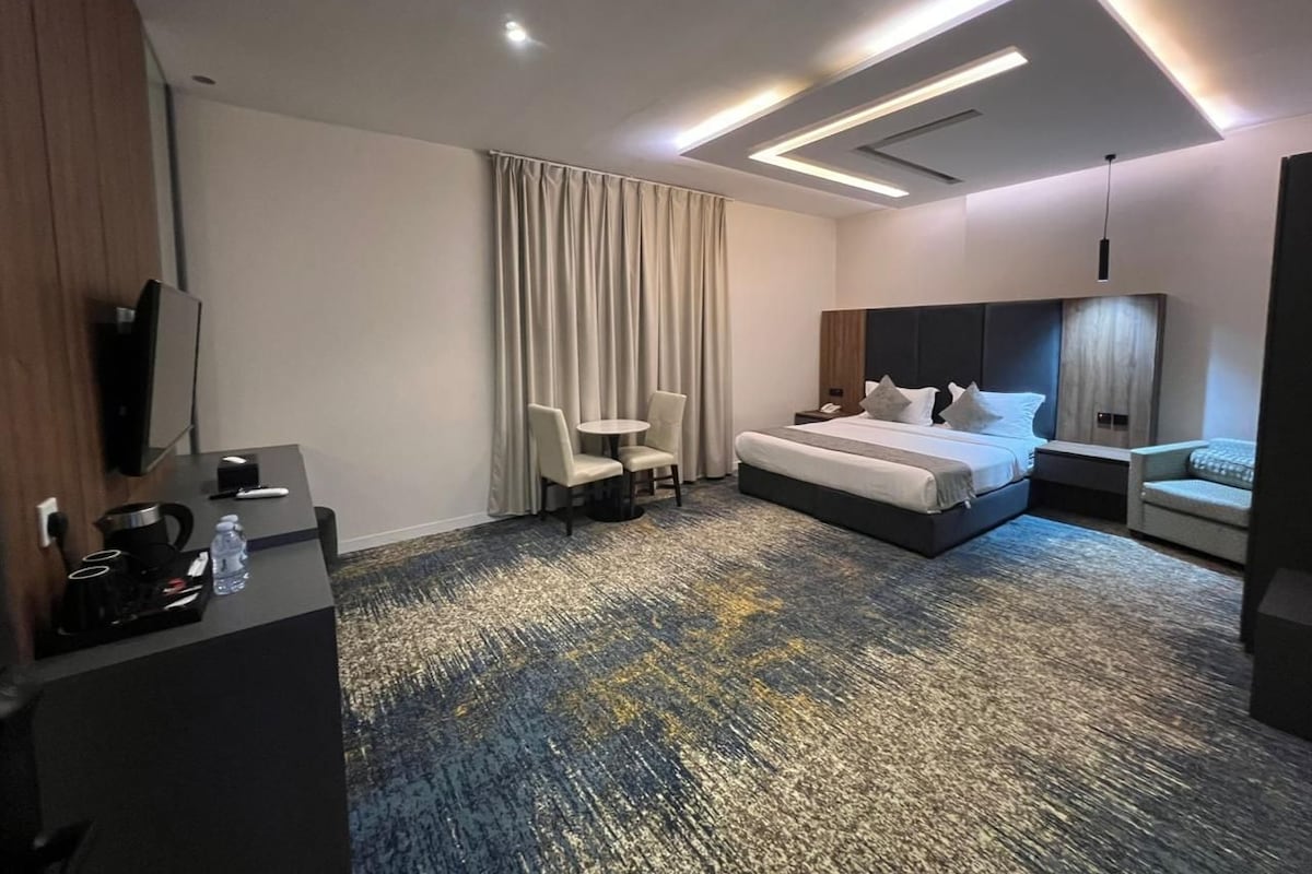Une chambre d’hôtel avec un lit, un bureau, une chaise, une télévision et une grande fenêtre avec des rideaux.