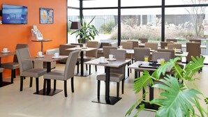 Un comedor moderno con mesas y sillas, un televisor en la pared y un amplio ventanal con vistas al exterior.