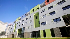 Un edificio de varios pisos con un diseño moderno, que cuenta con balcones, ventanas amplias y una pared verde decorativa.
