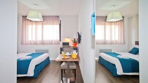 Habitación de hotel con dos camas individuales, una mesita con productos para el desayuno, un televisor y un espejo.