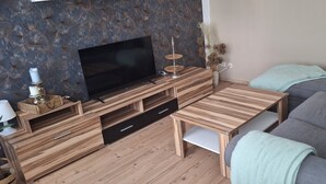 Ein modernes Wohnzimmer mit Flachbildfernseher, Holzmöbeln und einem grauen Sofa.