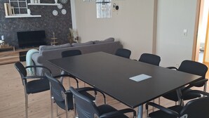 Ein Essbereich mit einem rechteckigen Tisch, acht Stühlen, einer Couch, einem Fernseher und dekorativen Gegenständen an der Wand.