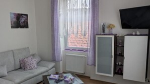 Un salon avec un canapé gris, une table basse, un meuble et un téléviseur fixé au mur.