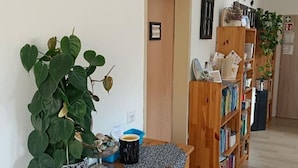 Une pièce avec une grande plante verte, une bibliothèque en bois et une petite table sur laquelle se trouvent une tasse et des objets décoratifs.