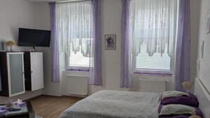 Une chambre à coucher avec un lit, une télévision, une armoire et une fenêtre avec des rideaux.