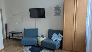 Un salon avec deux canapés bleus, un téléviseur, une armoire en bois et un tapis à motifs.