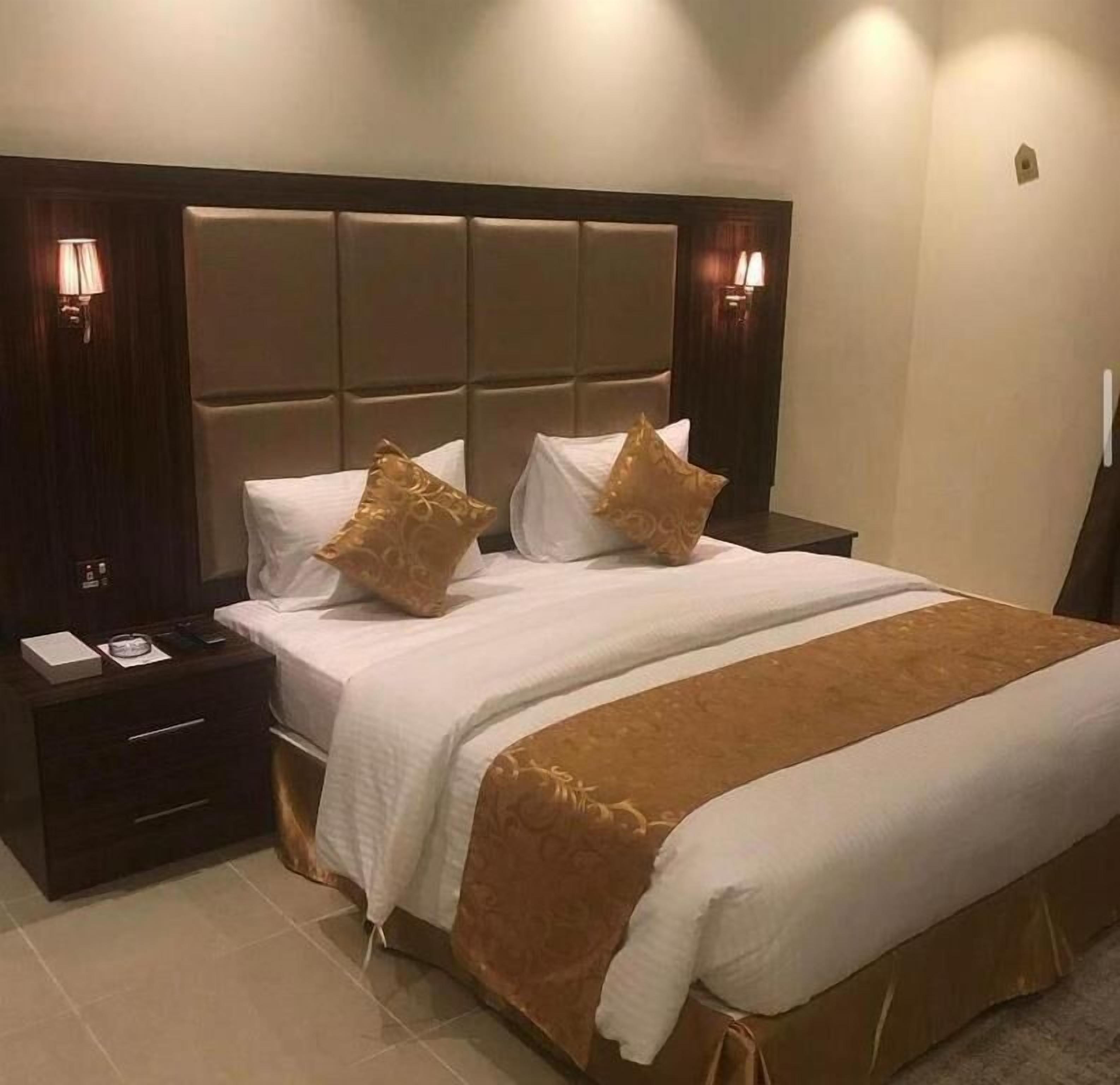 A hotel room with a large bed, a nightstand, and two wall-mounted lamps.