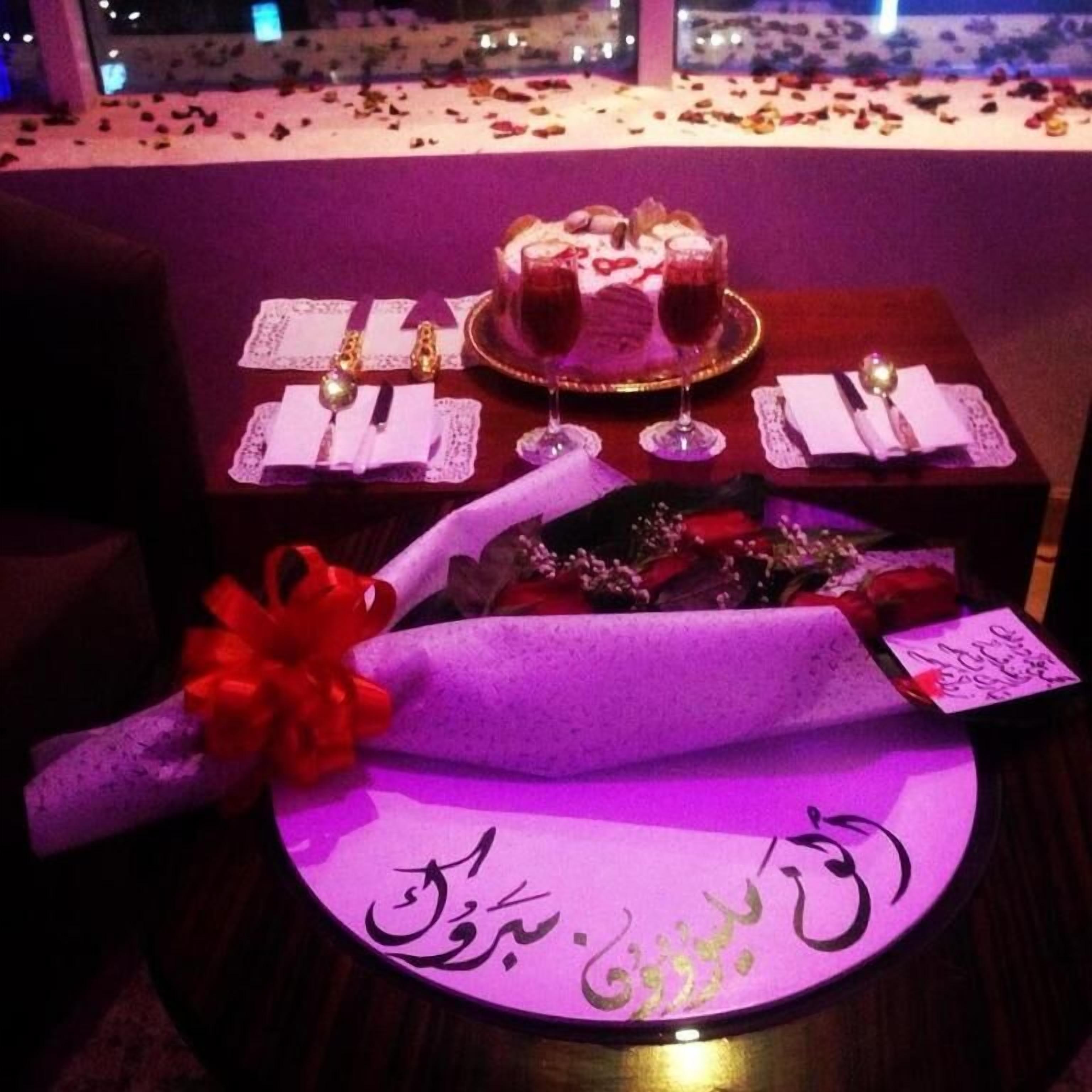 A romantic dinner setting with a table set for two, featuring a cake, wine glasses, and a decorative centerpiece.