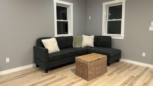 A modern living room with a dark grey sofa, white and green throw pillows, and a woven basket on a wooden floor.