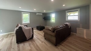 A living room with a brown leather couch, a black ottoman, and a grey wall with a mounted TV.