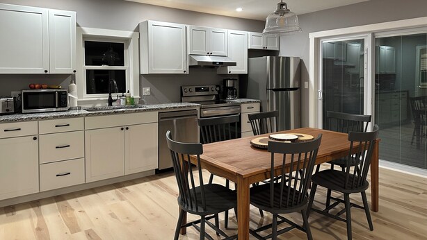 A modern kitchen with white cabinets, stainless steel appliances, and a wooden dining table with four chairs.
