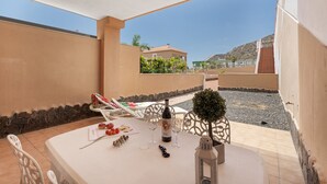 An outdoor dining area with a table set for two, a bottle of wine, and a small potted plant. - Brisas de Chasna Holiday Apartment with Sea Views, Shared Pool and Wi-Fi (Costa Adeje)