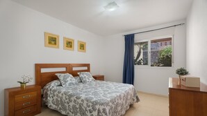 A bedroom with a bed, wooden nightstands, a dresser, a window with curtains, and three wall-mounted pictures. - Brisas de Chasna Holiday Apartment with Sea Views, Shared Pool and Wi-Fi (Costa Adeje)