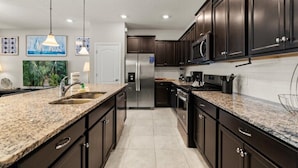 Una cocina moderna con armarios oscuros, encimeras de granito, electrodomésticos de acero inoxidable e iluminación colgante.