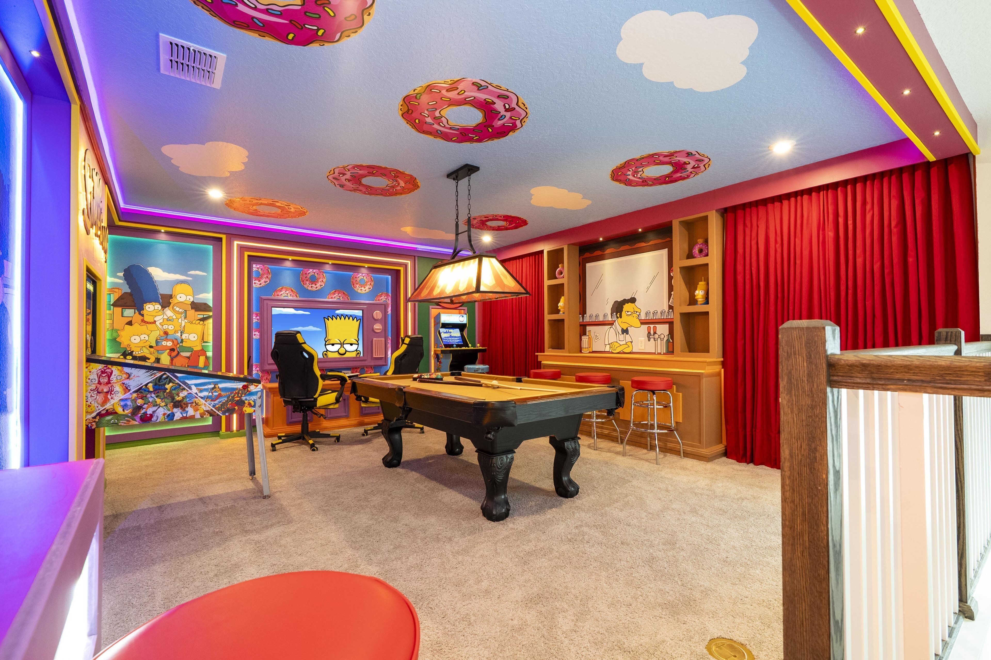 A room with a pool table, a bar area, and a Simpsons-themed wall.