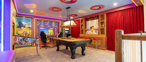 A room with a pool table, a bar area, and a Simpsons-themed wall.