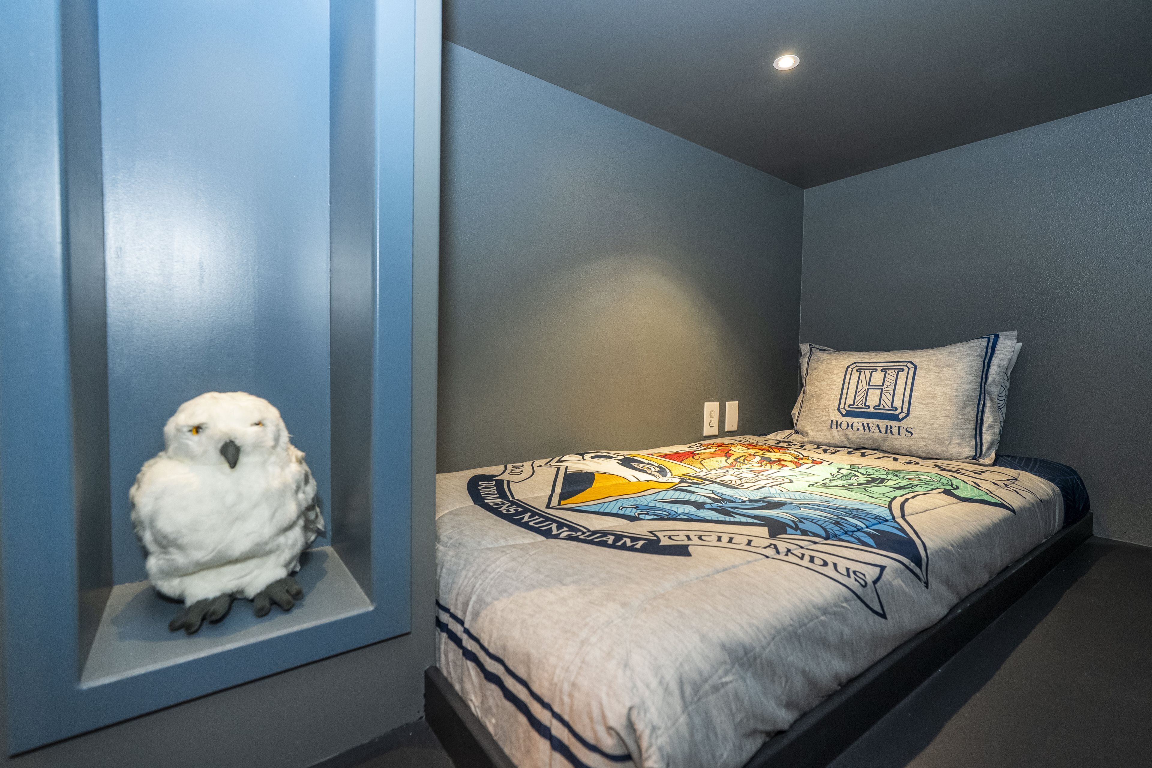 Un dormitorio con una cama que presenta un edredón con temática de Harry Potter, una almohada con el escudo de Hogwarts y una figura de búho montada en la pared.