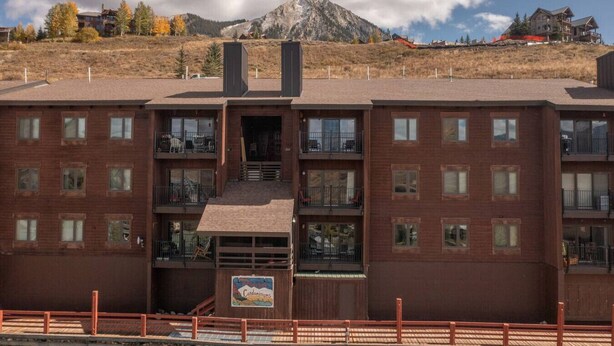 A multi-story brick building with balconies, a sign indicating 'Condominiums', and a mountainous backdrop. - The Elk Mountain Escape (Mt. Crested Butte)