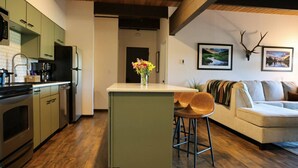 A modern kitchen with a central island, wooden flooring, and a dining area with a sofa and chairs. - The Elk Mountain Escape (Mt. Crested Butte)