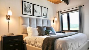 A bedroom with a large bed, a headboard, bedside tables, and a window with curtains. - The Elk Mountain Escape (Mt. Crested Butte)