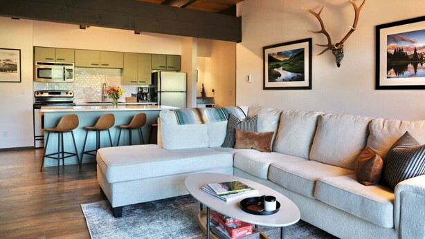 A modern living room with a sofa, coffee table, and a kitchen in the background. - The Elk Mountain Escape (Mt. Crested Butte)