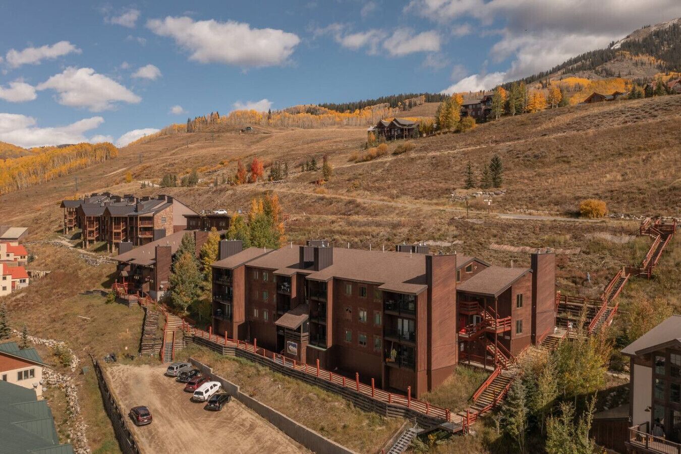 A modern multi-story building with a central courtyard, surrounded by a hilly landscape with autumn foliage.