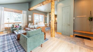 Un vaste salon doté d’un plafond avec une grande poutre en bois, d’une porte verte et offrant une vue sur l’extérieur grâce à de grandes fenêtres.