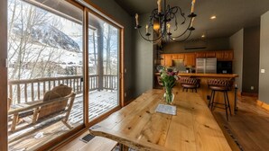 Un vaste espace dédié à la salle à manger, avec une grande table en bois, un lustre et une vue sur une terrasse enneigée.