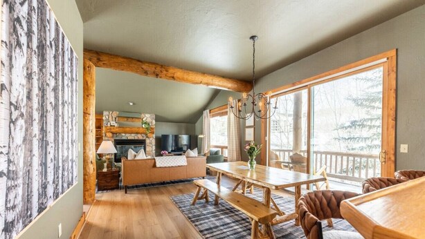 Un salon chaleureux avec une cheminée, des meubles en bois et de grandes fenêtres donnant sur l’extérieur.