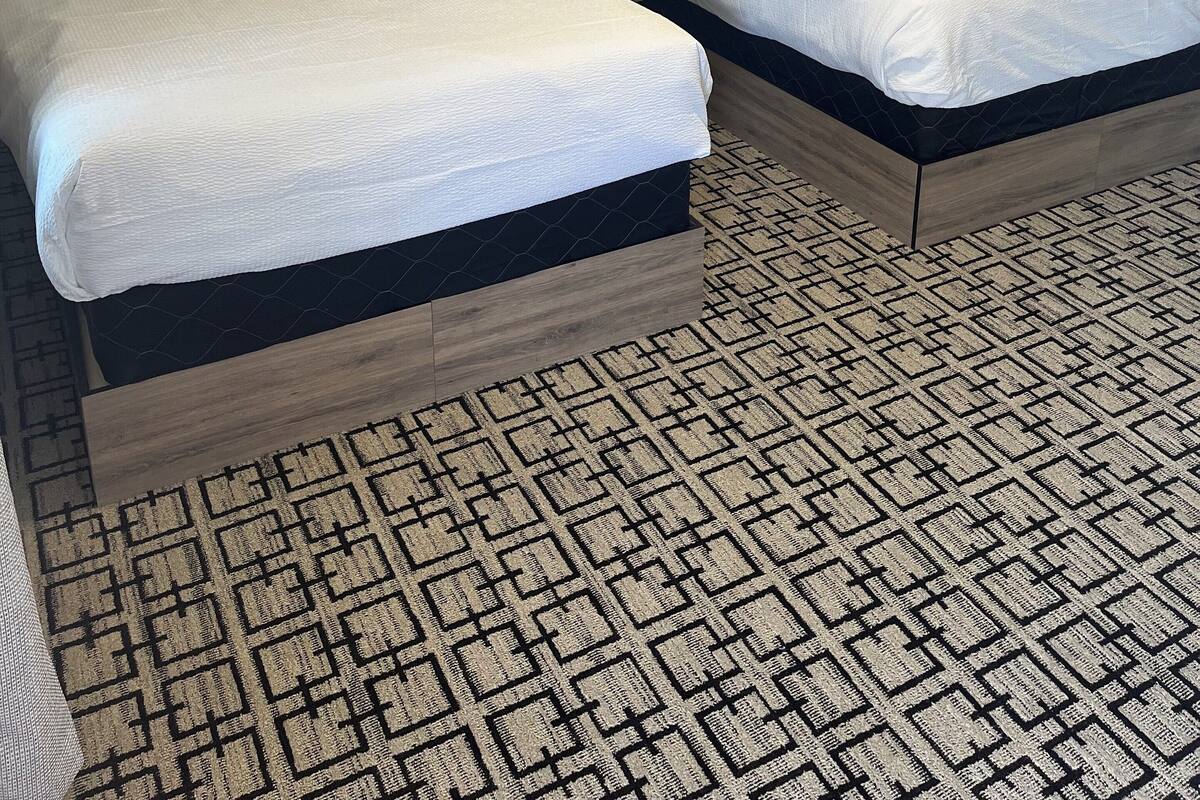 A hotel room with two beds, a patterned carpet, and a ceiling light.