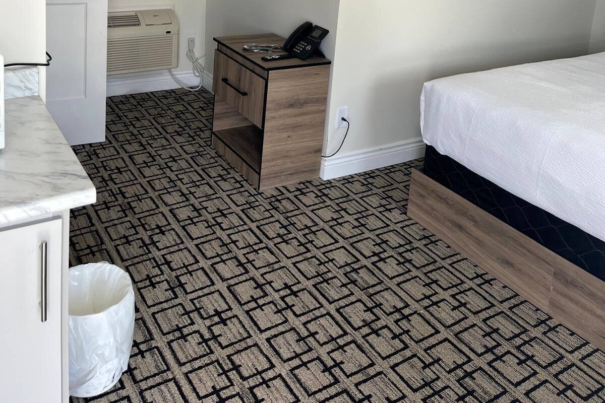 A small, neatly arranged bedroom with a bed, a bedside table with a phone, a radiator, and a patterned carpet.